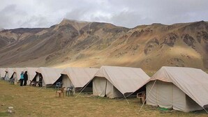 Varias tiendas de campaña en una zona montañosa, con gente de pie cerca.