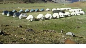 Varias tiendas de campaña dispuestas en filas sobre un campo de hierba, con montañas al fondo.