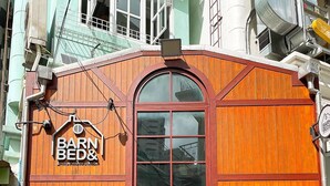 A building with a wooden facade, a large arched window, and a sign reading "BARN&BED". - Barn and Bed Hostel (Bangkok)