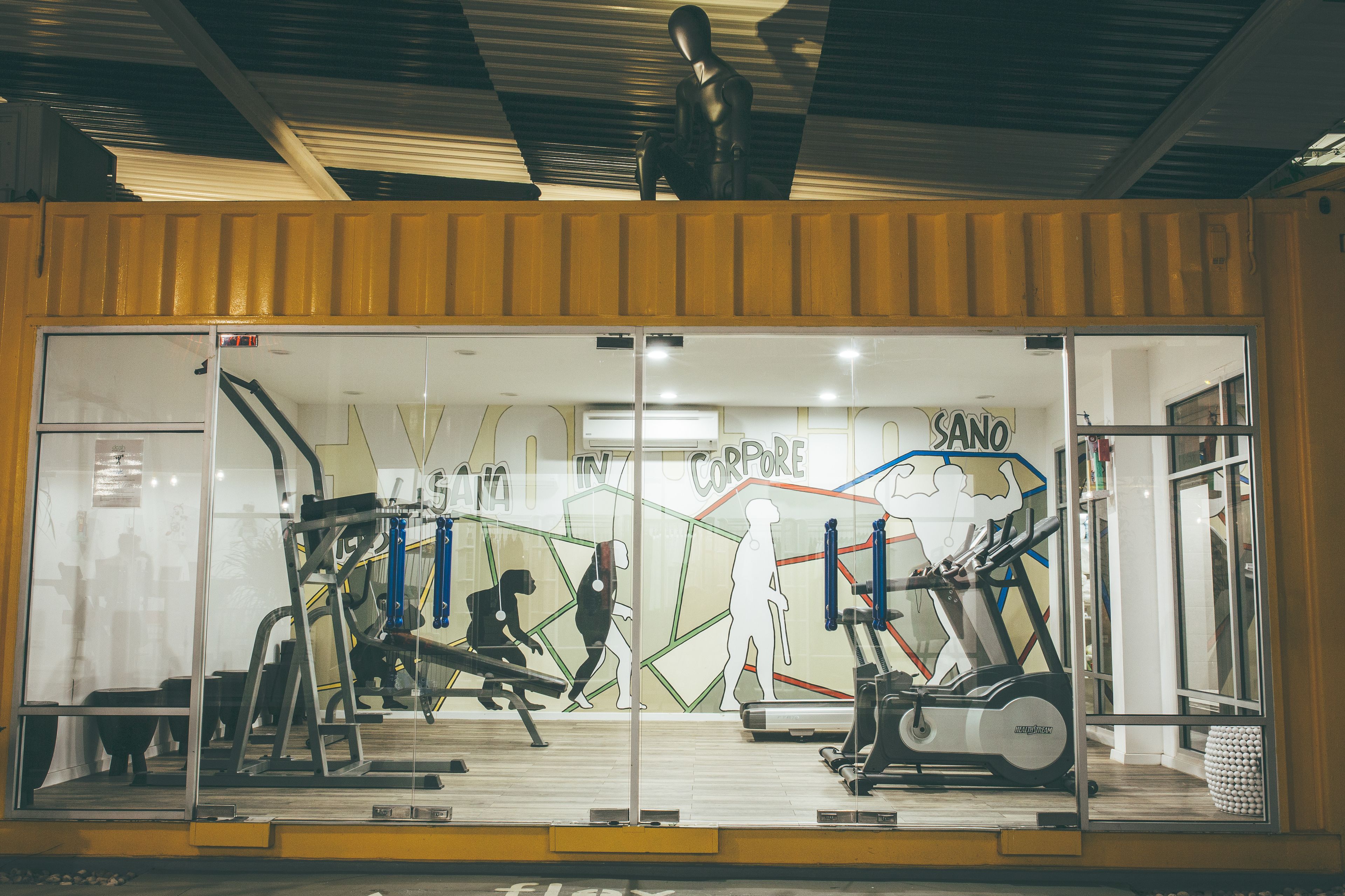A gym with exercise equipment, a mirrored wall, and a large window.