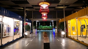 A covered walkway with a central red light fixture, potted plants, and glass-fronted shops on either side. - Dash Box Hotel Cyberjaya (Cyberjaya)