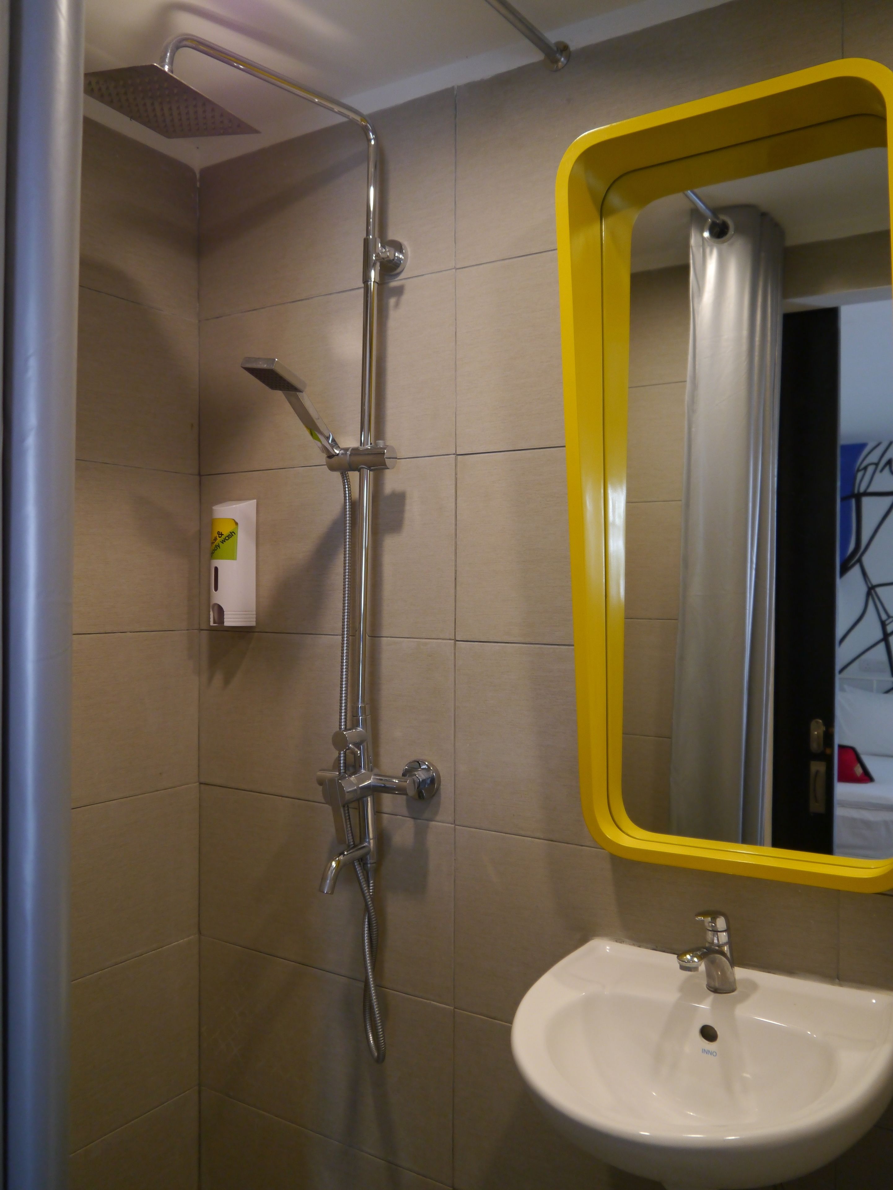 A bathroom with a shower, a sink, and a mirror with a yellow frame.