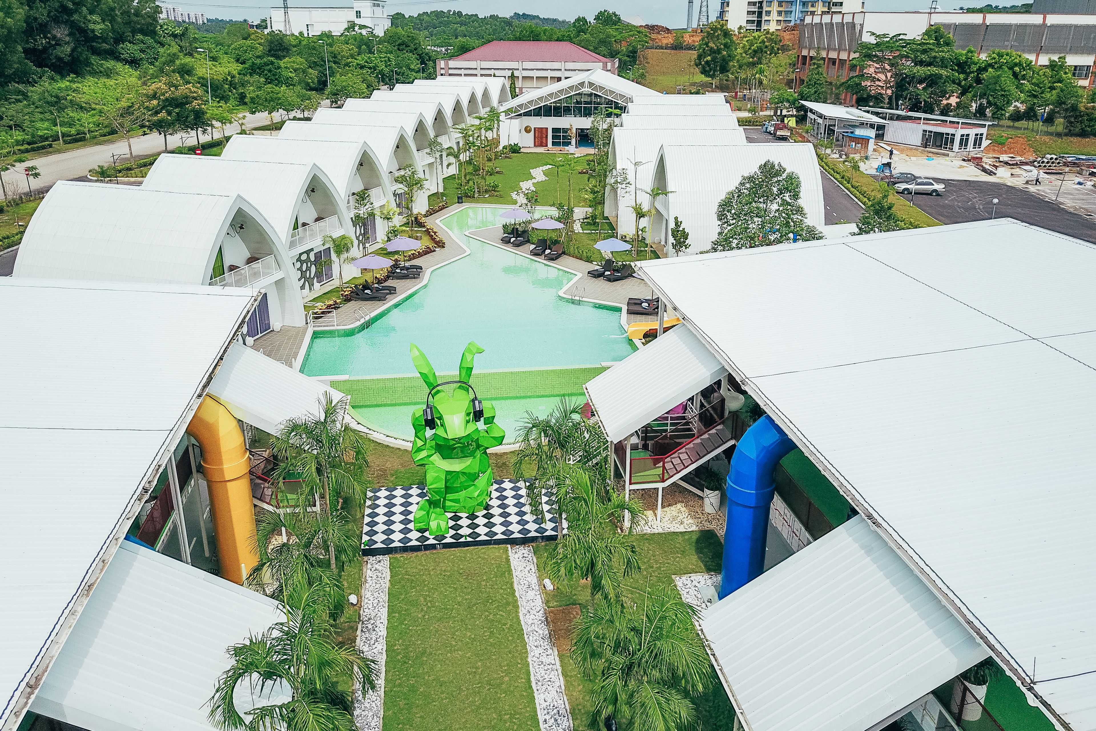 Een resort met een zwembad, een groot groen kunstwerk en meerdere gebouwen met witte daken.