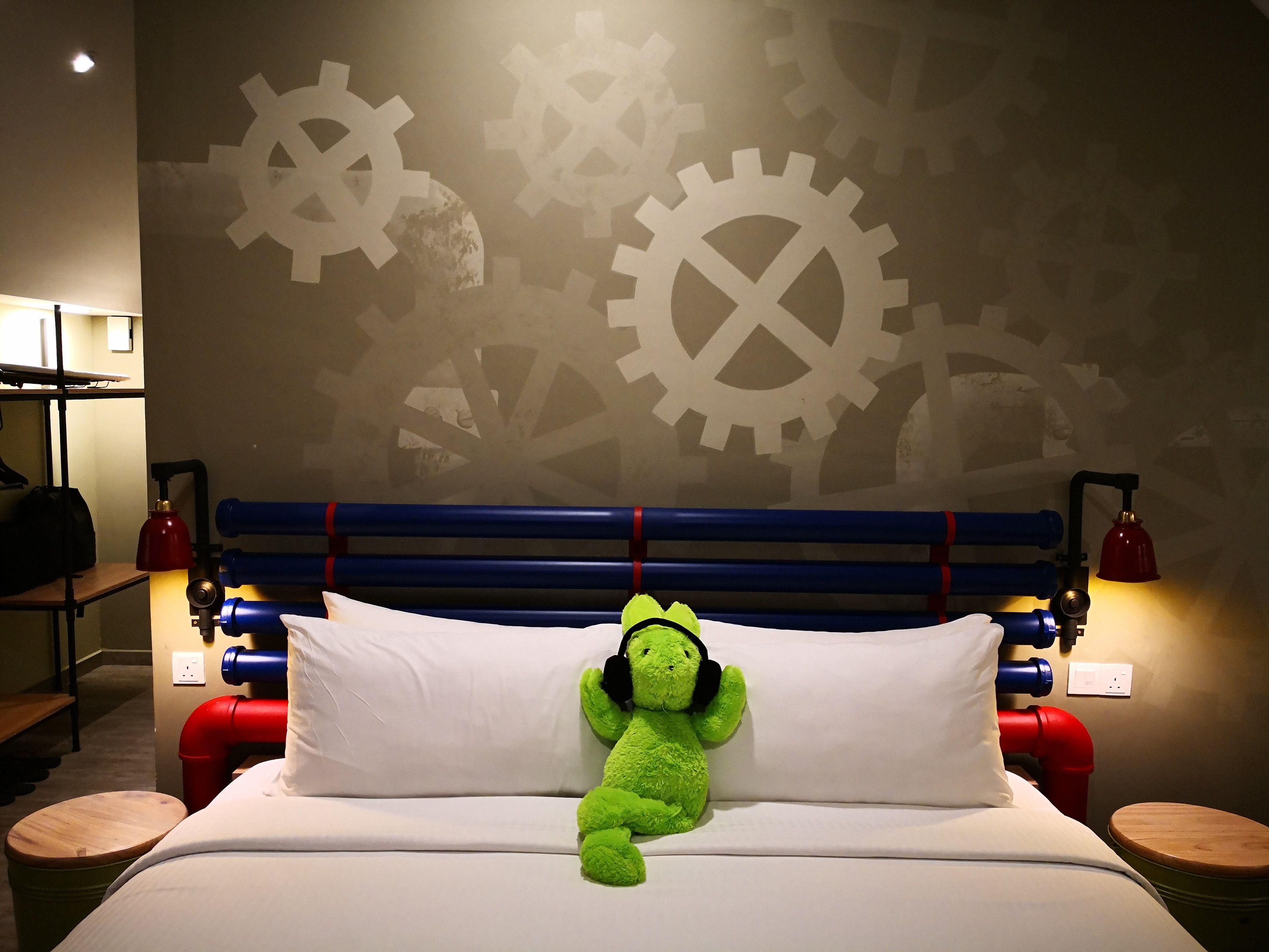 Una cama con un peluche verde, almohadas blancas y un cabecero azul.