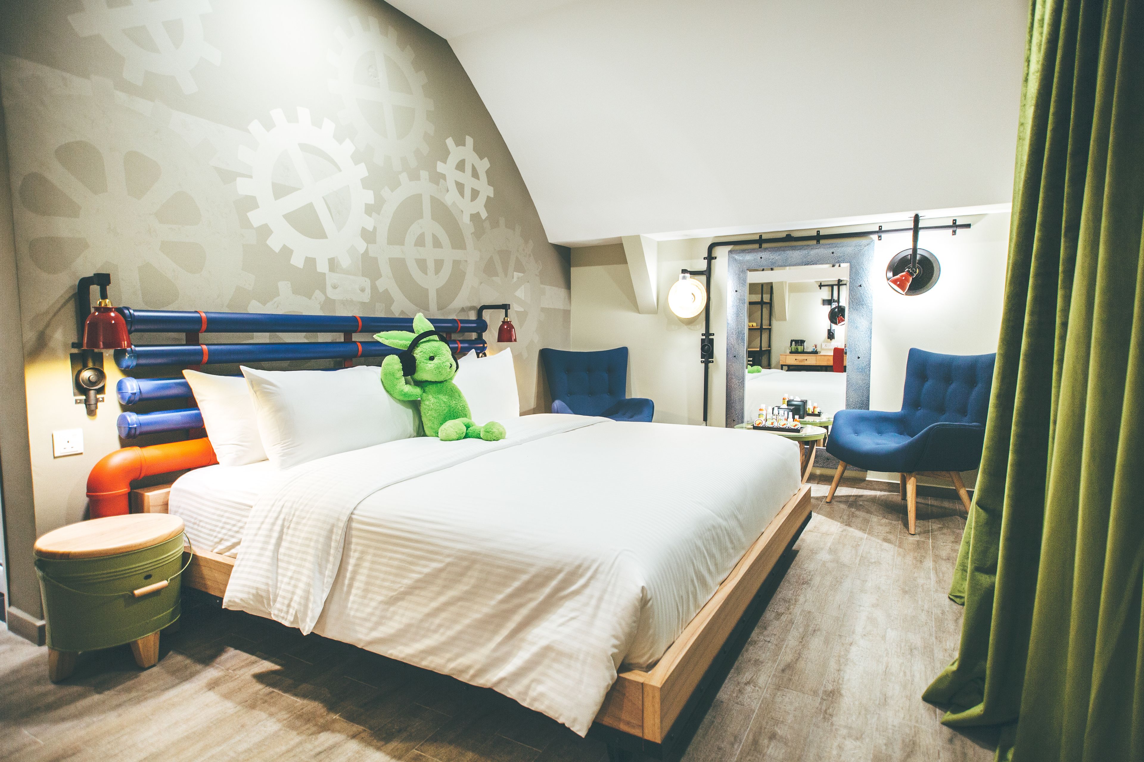 A bedroom with a bed, a green plush toy, a blue chair, and a wooden nightstand.
