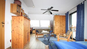 A spacious room with a bed, a sofa, a chair, a dining table, and a ceiling fan. - B&B am See - Privatzimmer (Cologne)
