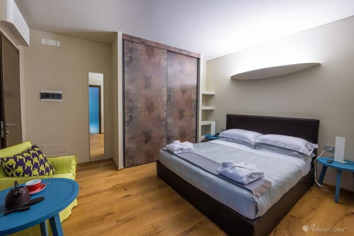 Moderni hotellihuone, jossa on sänky, sininen pyöreä pöytä, vihreä sohva ja puulattia.