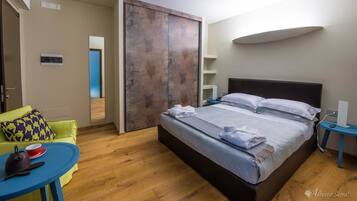 Une chambre d’hôtel moderne avec un lit, une table ronde bleue, un canapé vert et un plancher en bois.