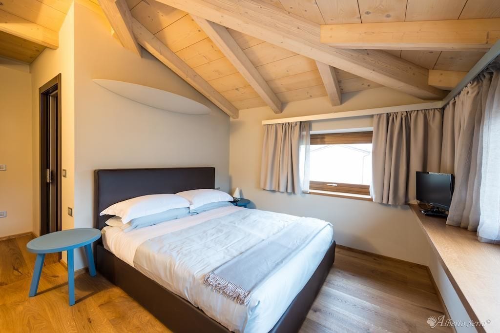 Une chambre à coucher avec un lit, une petite table, un téléviseur et une fenêtre avec des rideaux.