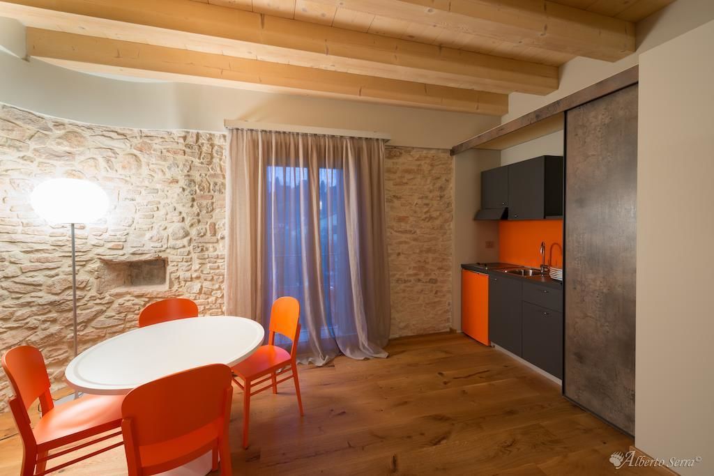 Un comedor con una mesa redonda y sillas naranjas, una pared de piedra y una cocina con armarios grises.