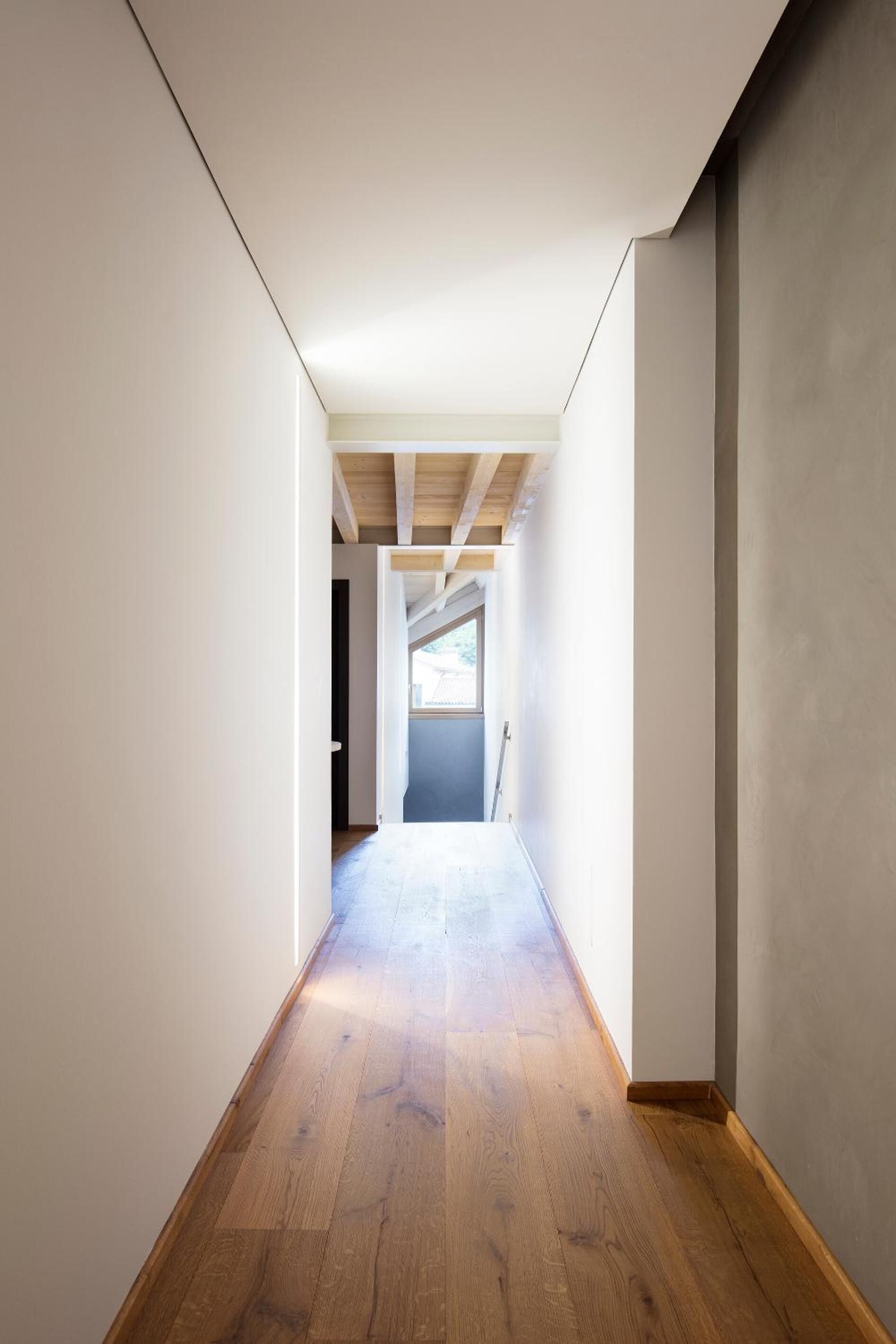 Un couloir étroit, au sol en bois, aux murs blancs et au plafond en pente.
