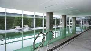 An indoor swimming pool with clear glass walls, lounge chairs, and a view of greenery outside. - The Lotus Hotel Chongqing (Chongqing)