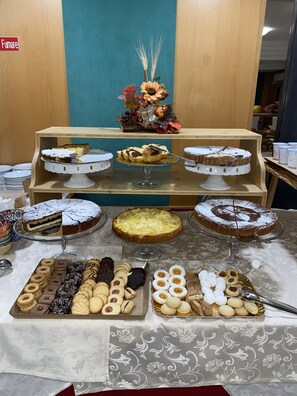 A buffet with various desserts and pastries, including cakes and cookies, displayed on a table with a patterned tablecloth.