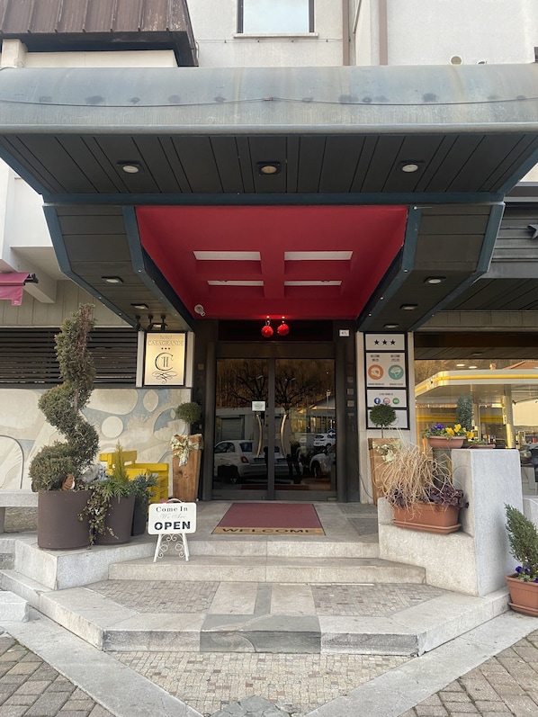 A hotel entrance with a red awning, a welcome mat, and potted plants.