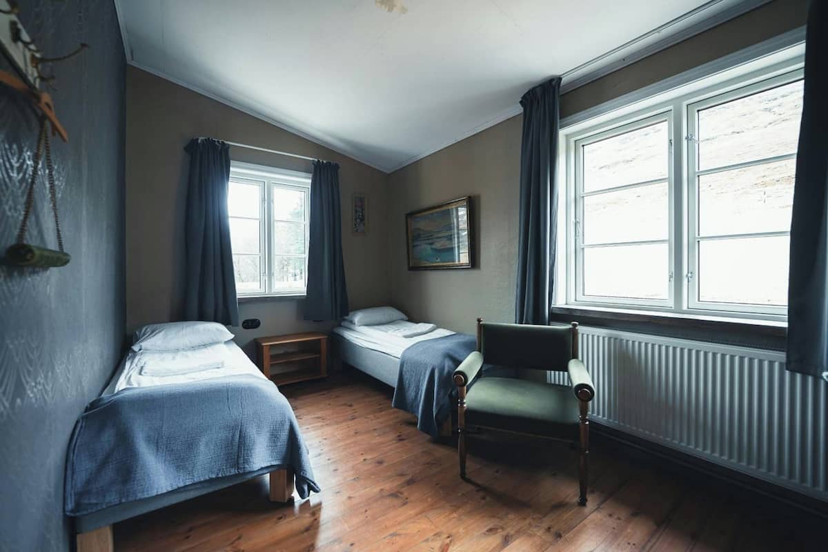 A room with two beds, a chair, a window, and a radiator.
