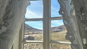 Una ventana con cortinas de encaje, vista a un paisaje rural y una estructura de madera al fondo.