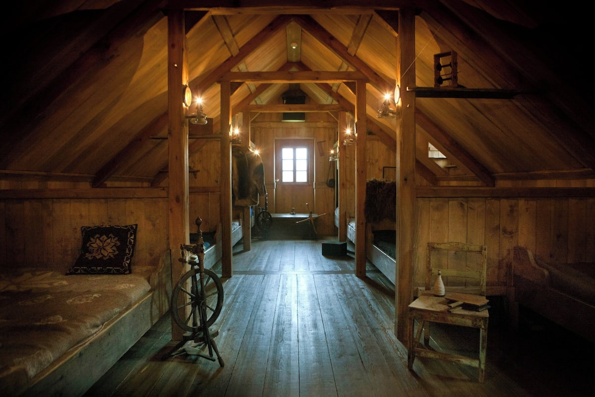 A wooden attic bedroom with a sloped ceiling, a bed, a chair, and a table.