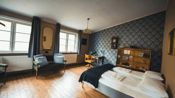 A room with a bed, a desk, a chair, a radiator, and a window with curtains.