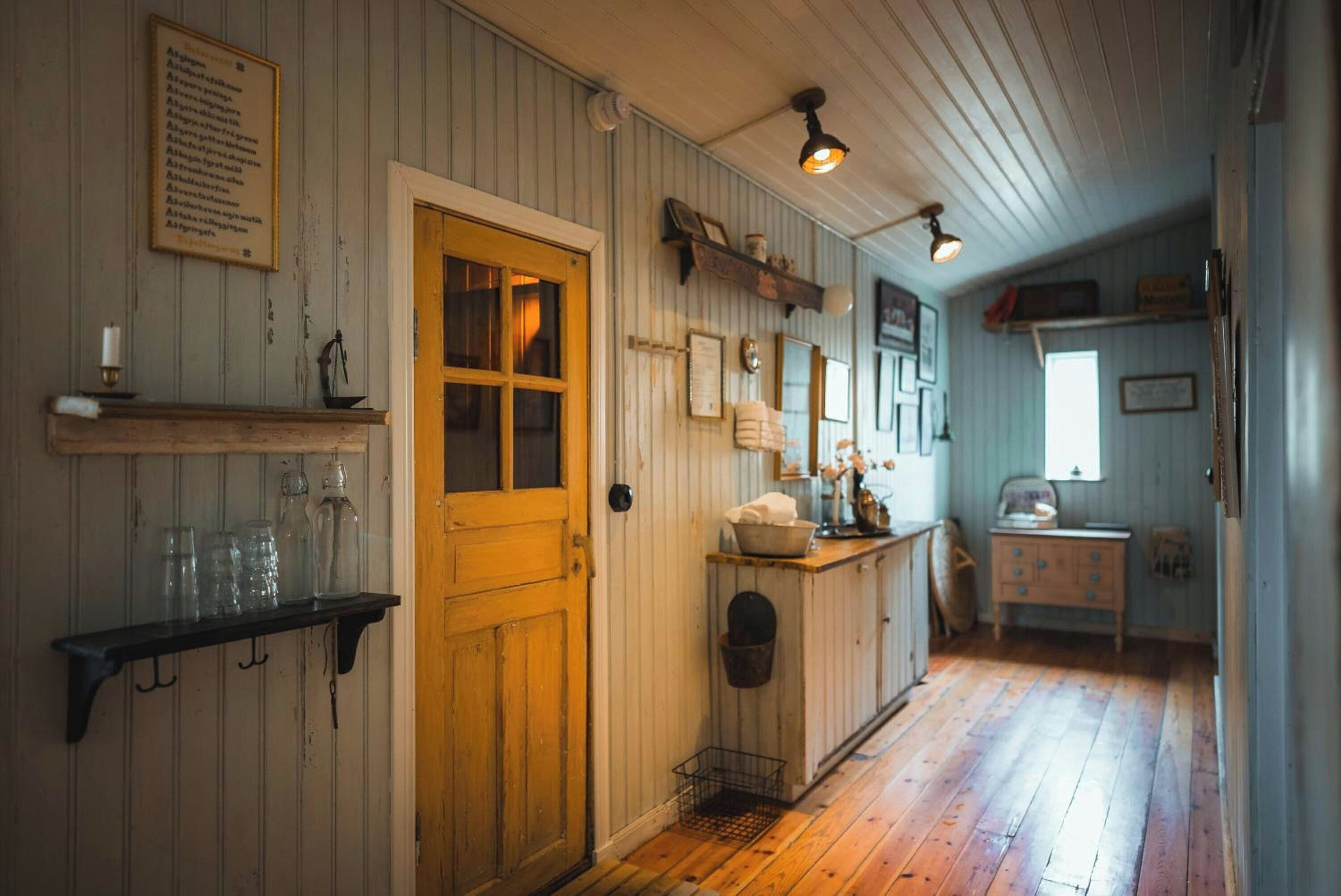Un intérieur rustique avec un plancher en bois, une porte en bois, une étagère remplie de bouteilles en verre et un luminaire suspendu.
