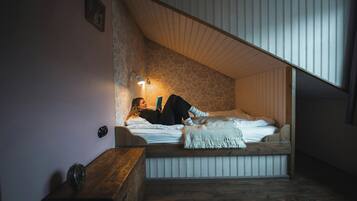 Un dormitorio acogedor con techo inclinado, una cama con edredón blanco, una lámpara de noche y una mesita de noche de madera.