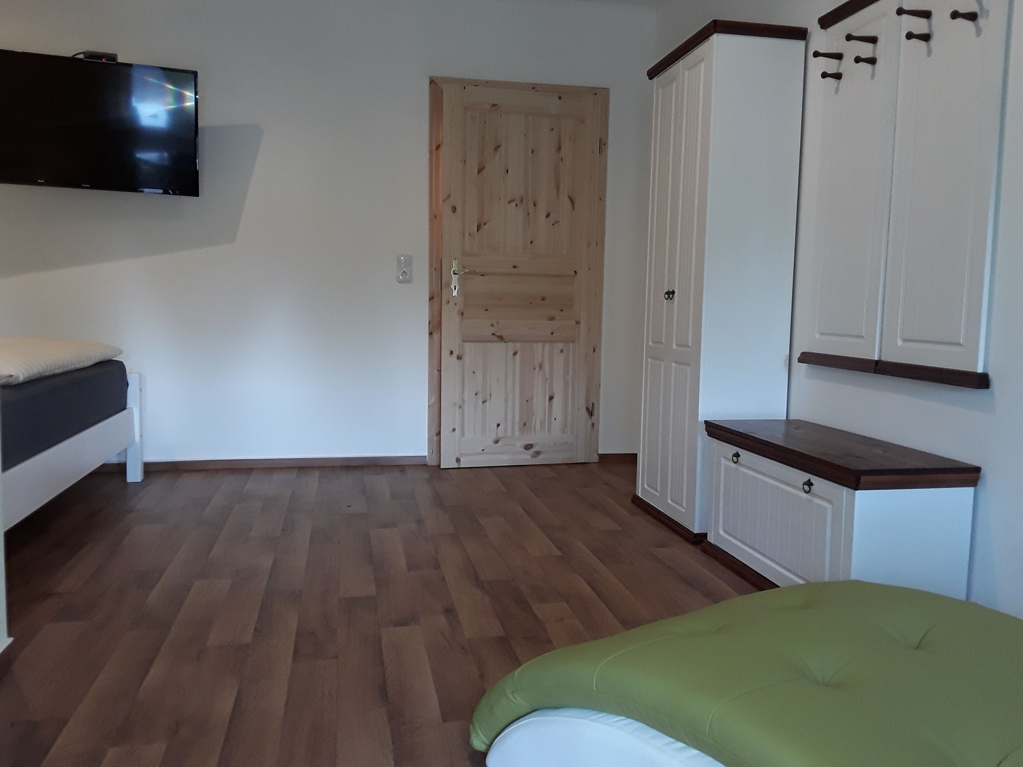 A room with a bed, a TV mounted on the wall, a wooden door, and a wardrobe.