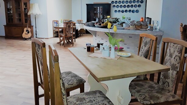 A dining area with a wooden table and chairs, a kitchen in the background, and a guitar on the floor.