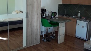 A compact room with a bed, a kitchenette, and a dining area with green chairs.