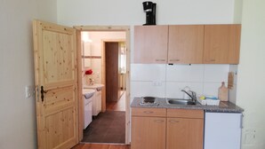 A compact kitchen with wooden cabinets, a sink, a coffee machine, and a small refrigerator.