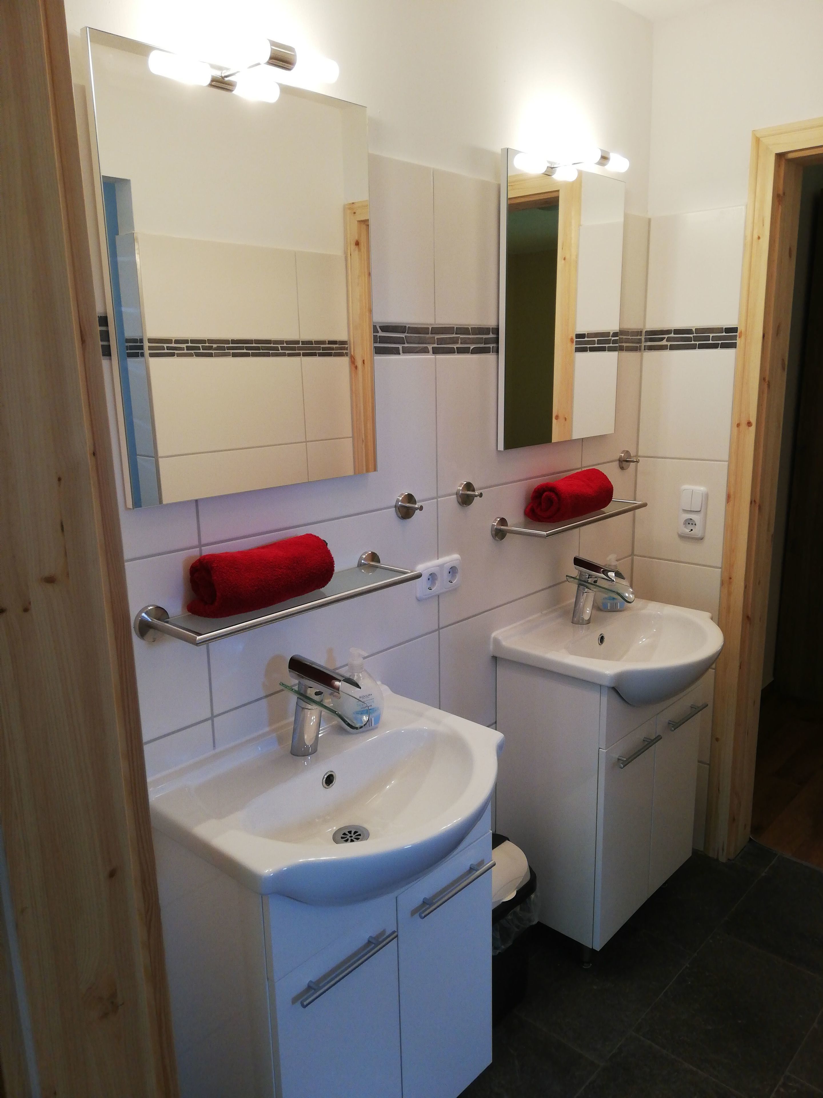 Une salle de bain avec deux lavabos, un miroir au-dessus de chacun, et une serviette rouge sur le lavabo de gauche.