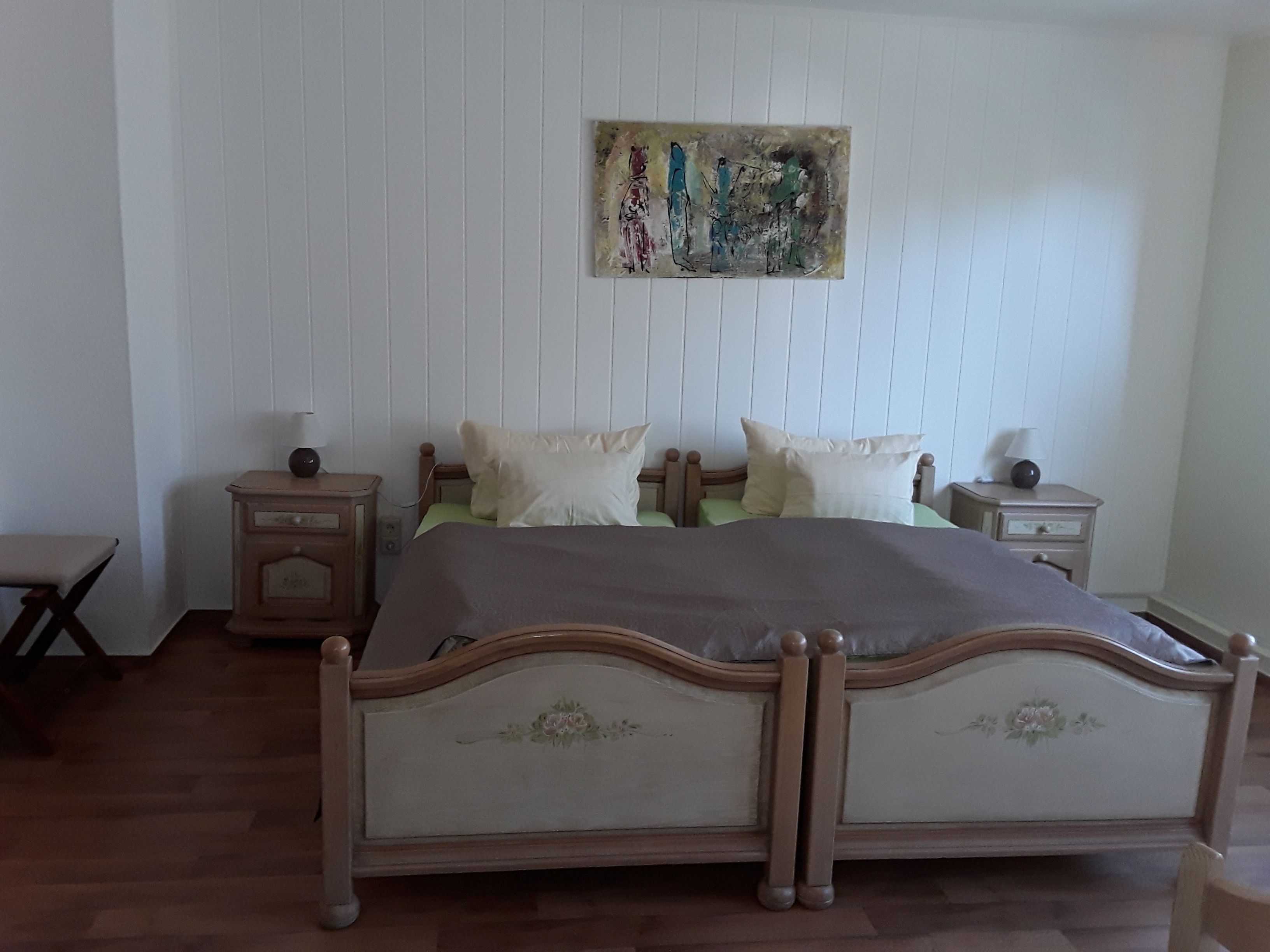 A bedroom with a wooden bed, two bedside tables, a nightstand, a chair, and a painting on the wall.