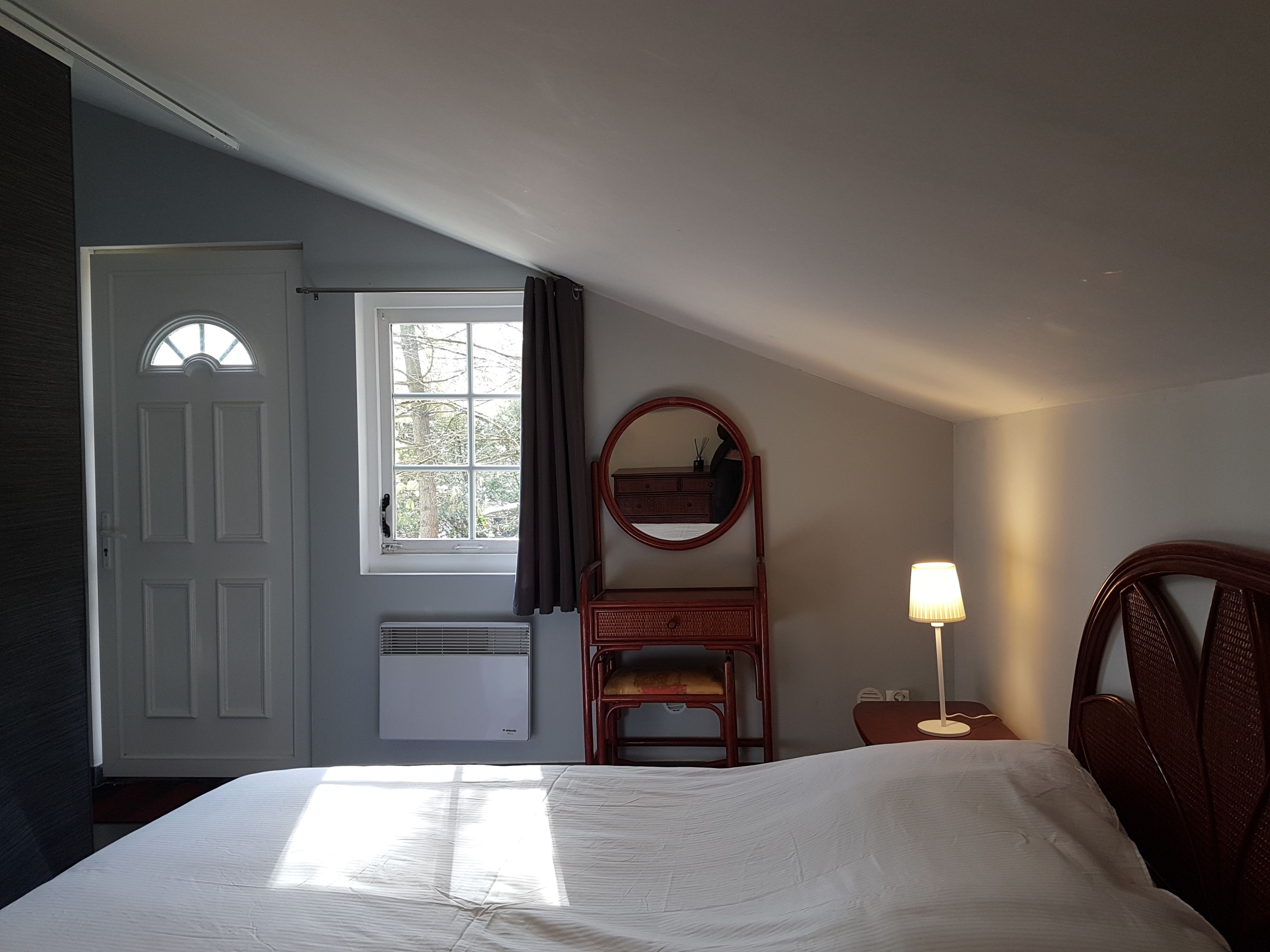 A bedroom with a bed, a dresser, a mirror, a lamp, and a window with curtains.