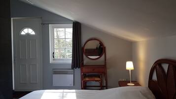 A bedroom with a bed, a dresser, a mirror, a lamp, and a window with curtains.