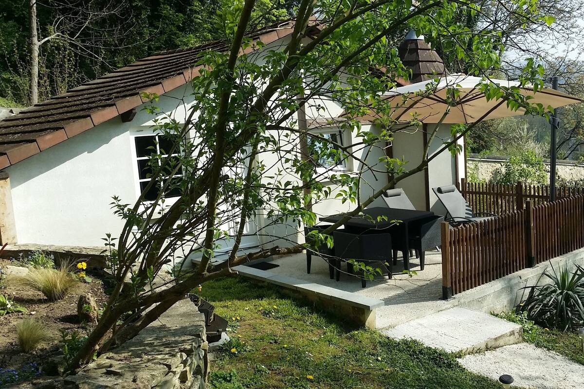 Una pequeña casa con un patio, un comedor con sillas y un jardín cercado.