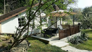 Une petite maison avec un patio, un coin repas avec des chaises et un jardin clôturé.
