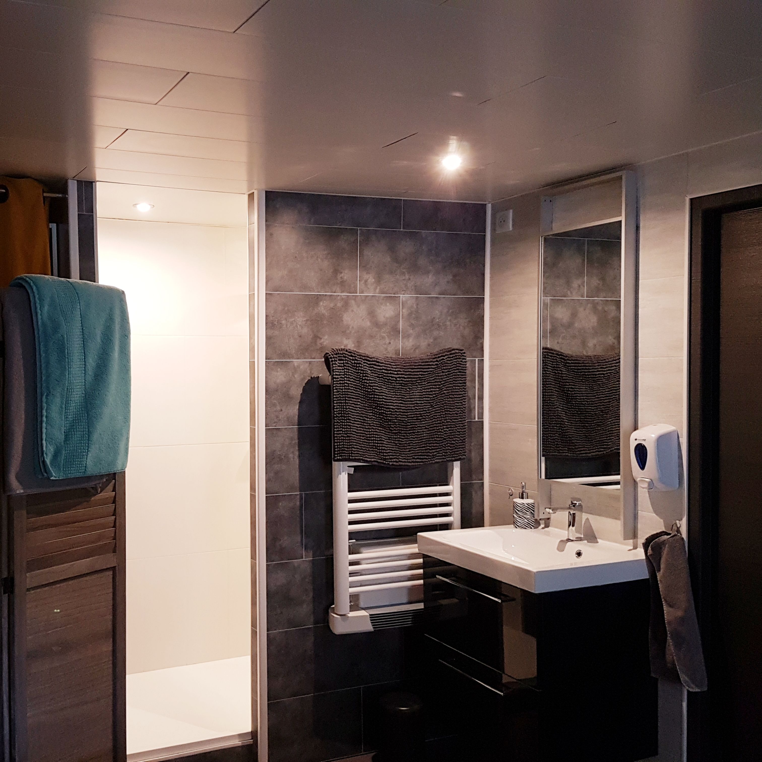 Une salle de bain moderne avec un lavabo blanc, des carreaux foncés, un porte-serviettes et un miroir.