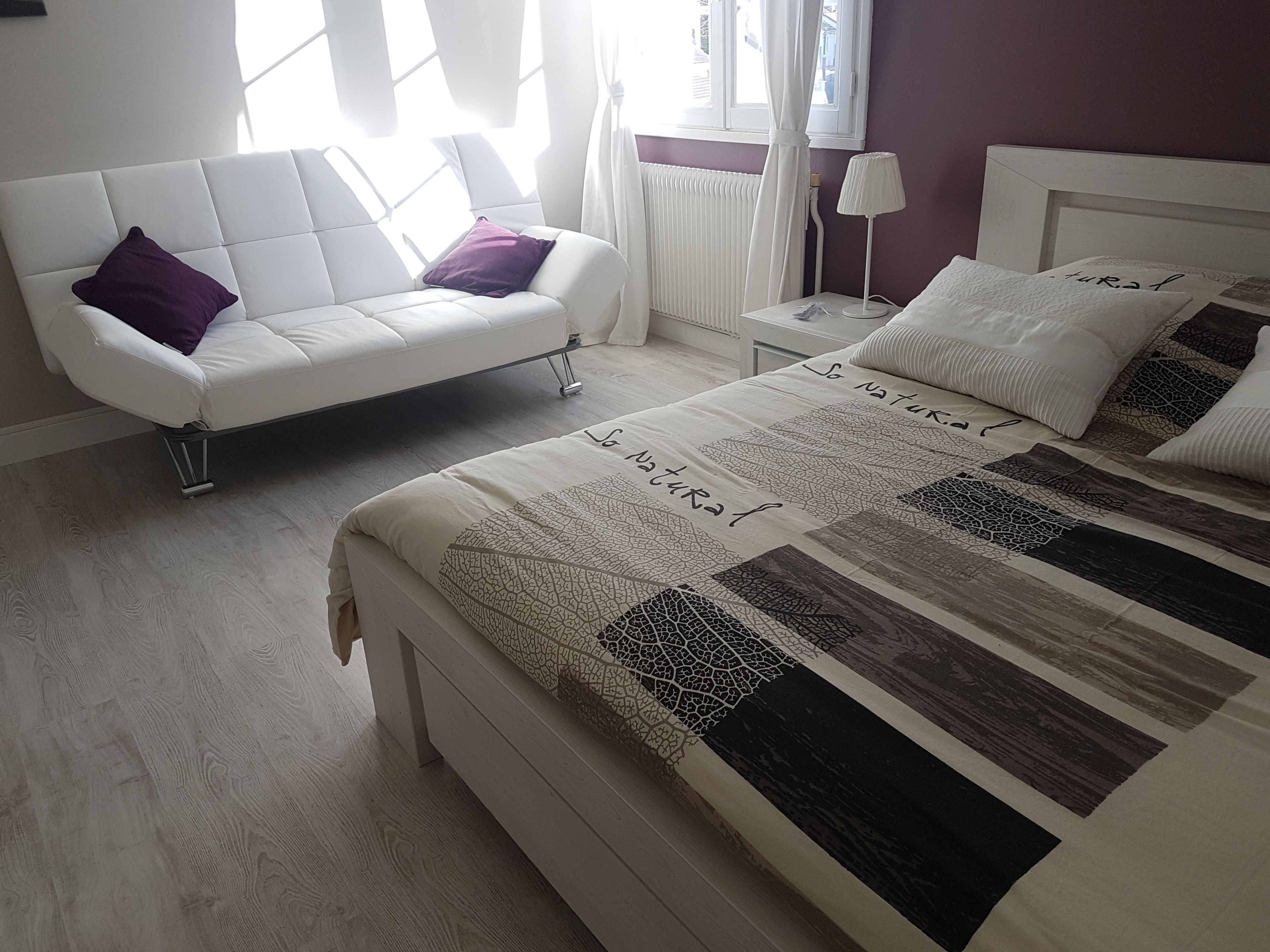 A bedroom with a bed, a white sofa, a nightstand, and a window with curtains.