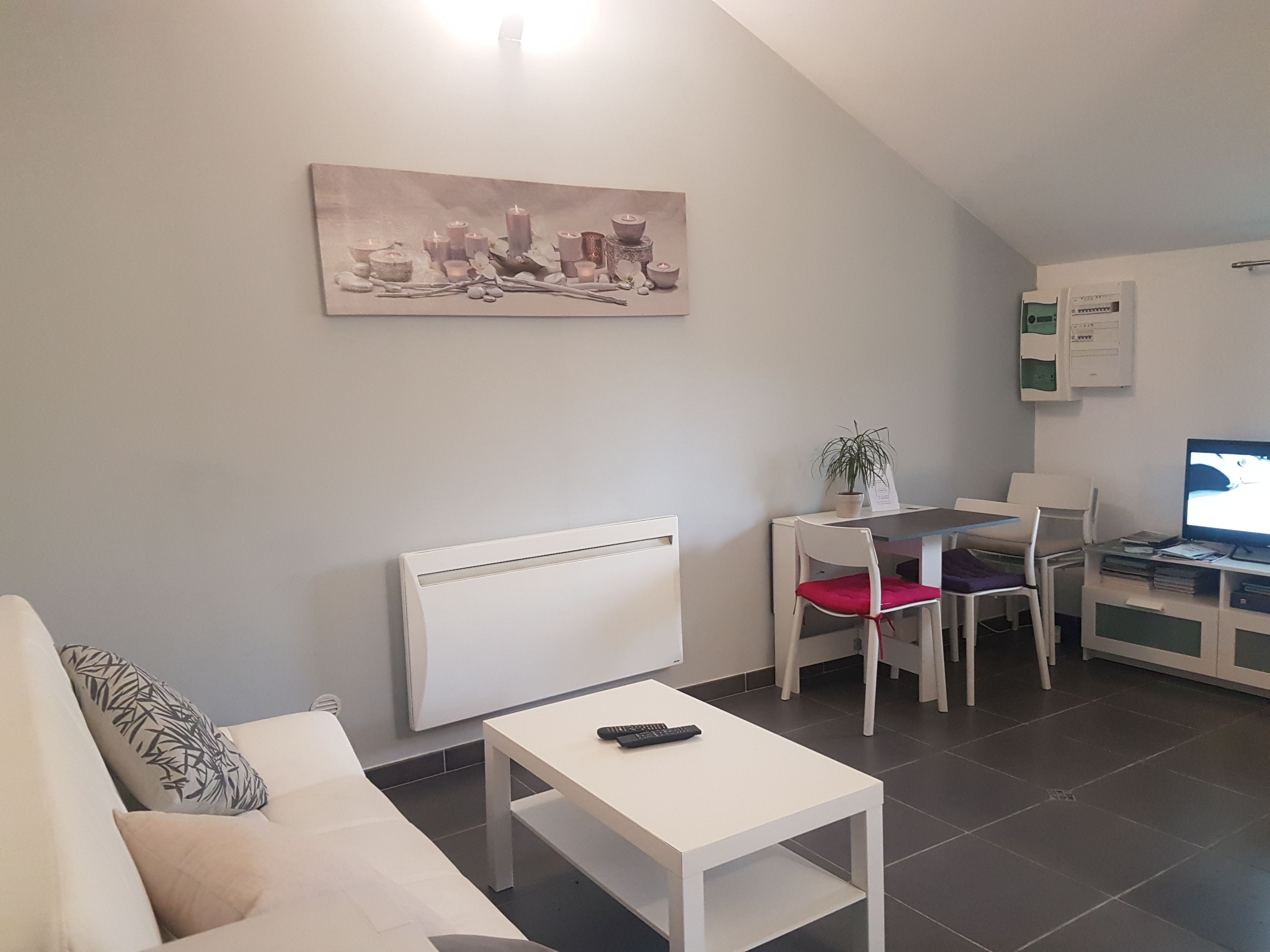 Un salon moderne avec un canapé blanc, une petite table blanche, un fauteuil rouge, un bureau blanc avec un ordinateur et un tableau accroché au mur.
