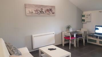 Un salon moderne avec un canapé blanc, une petite table blanche, un fauteuil rouge, un bureau blanc avec un ordinateur et un tableau accroché au mur.