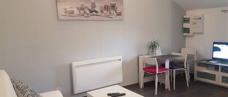 A modern living room with a white sofa, a small white table, a red chair, a white desk with a computer, and a painting on the wall.