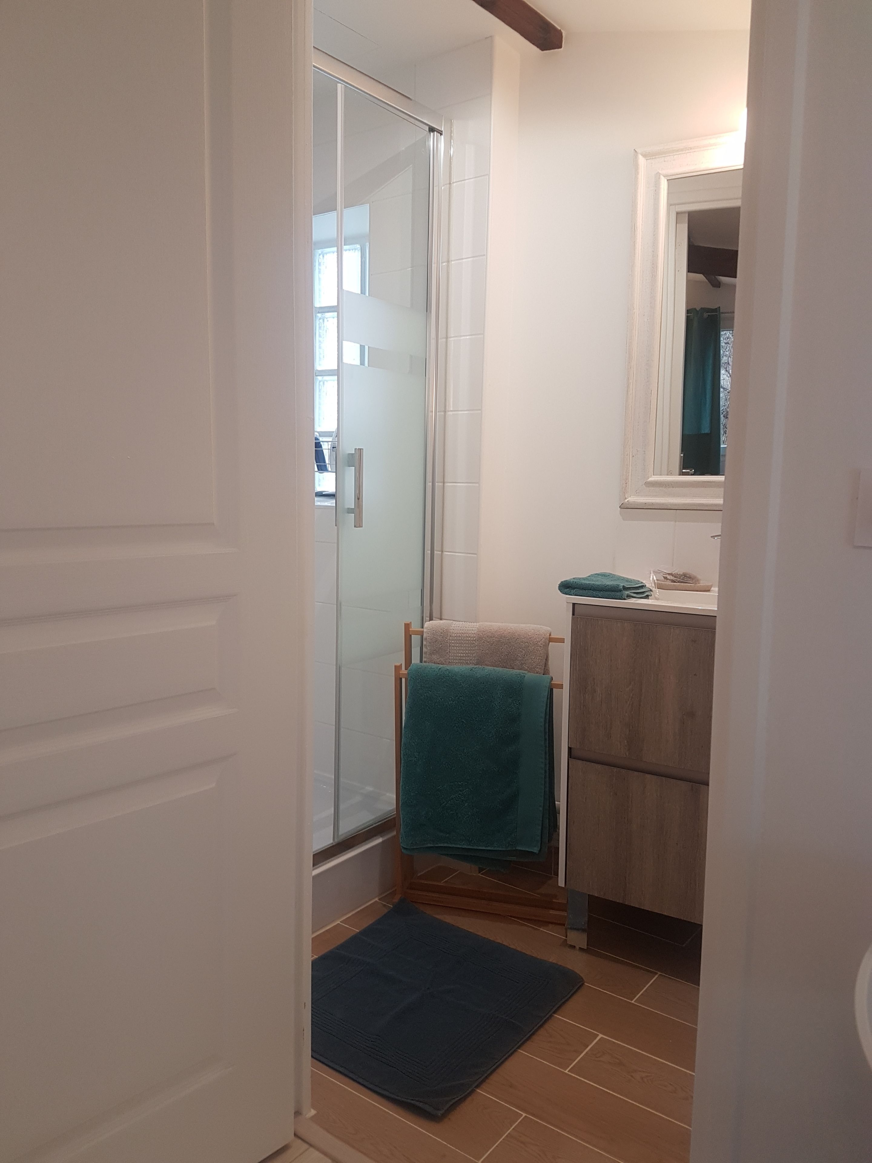 Une salle de bain avec une porte de douche en verre, un meuble en bois, un lavabo et une serviette bleue posée sur un porte-serviettes.