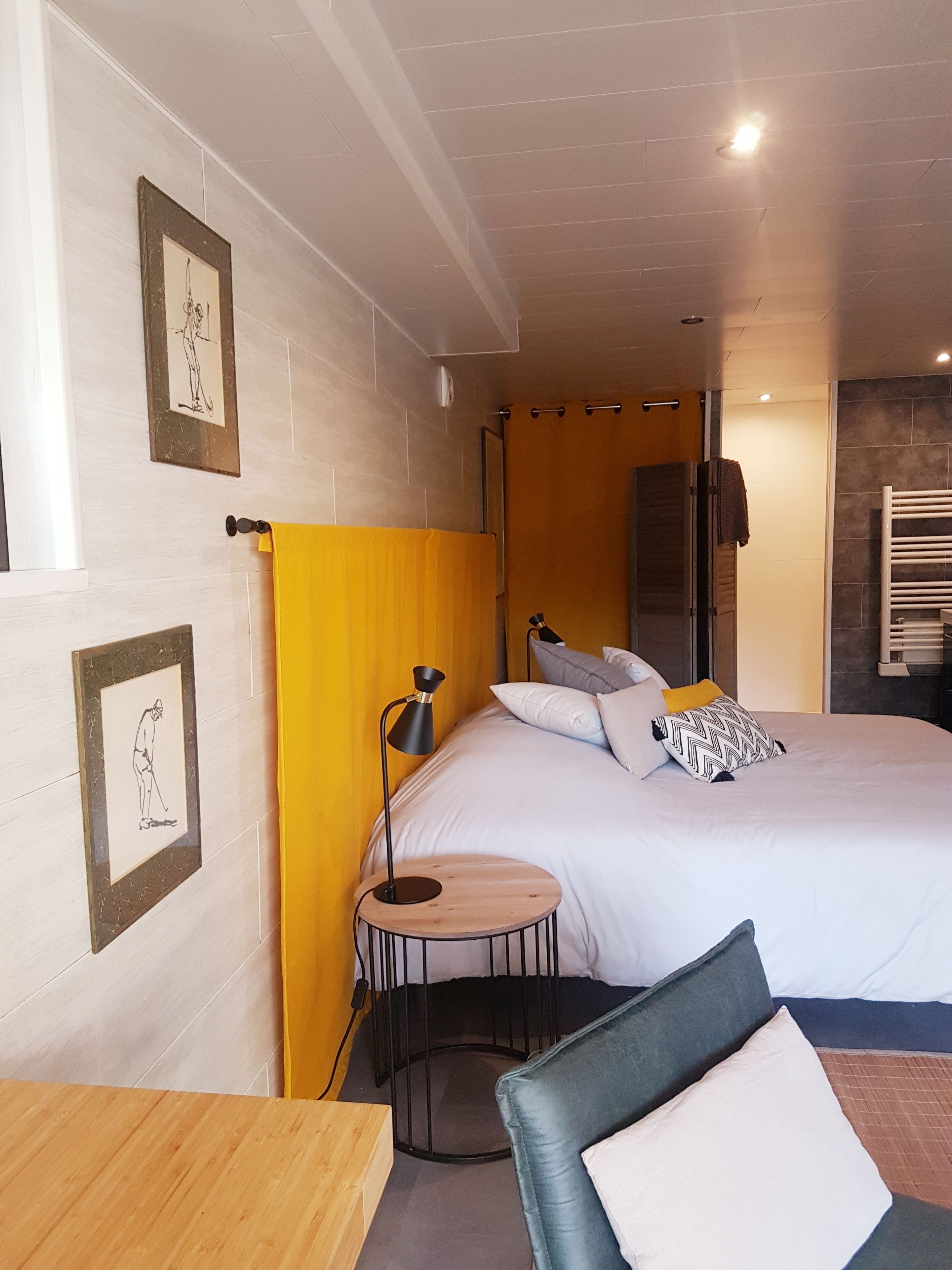 Een hotelkamer met een bed, een rond houten bijzettafeltje, een zwarte vloerlamp en een stoel.