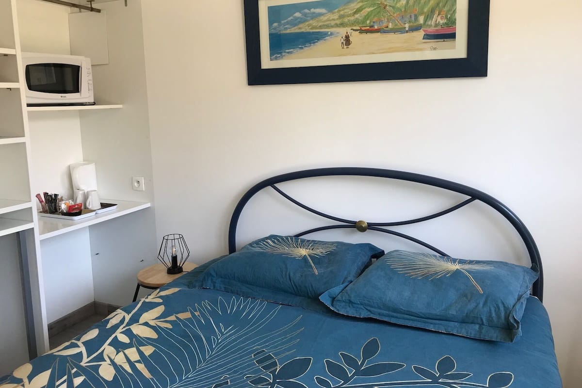 Une chambre avec un lit, une étagère sur laquelle se trouve un micro-ondes, et un tableau encadré accroché au mur.