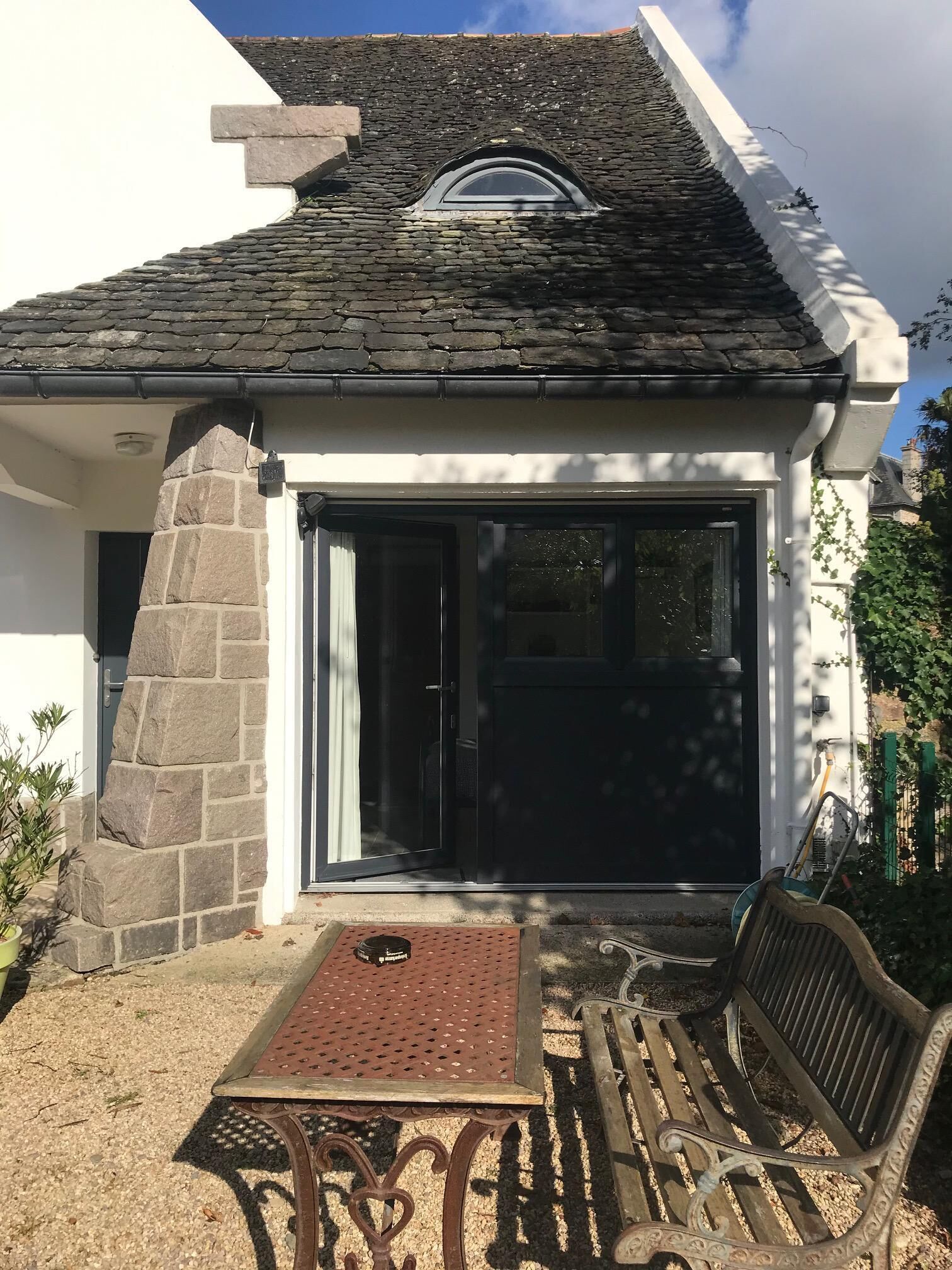 Un bâtiment revêtu de pierres, doté d’une grande porte vitrée et d’un petit espace porche avec un banc.