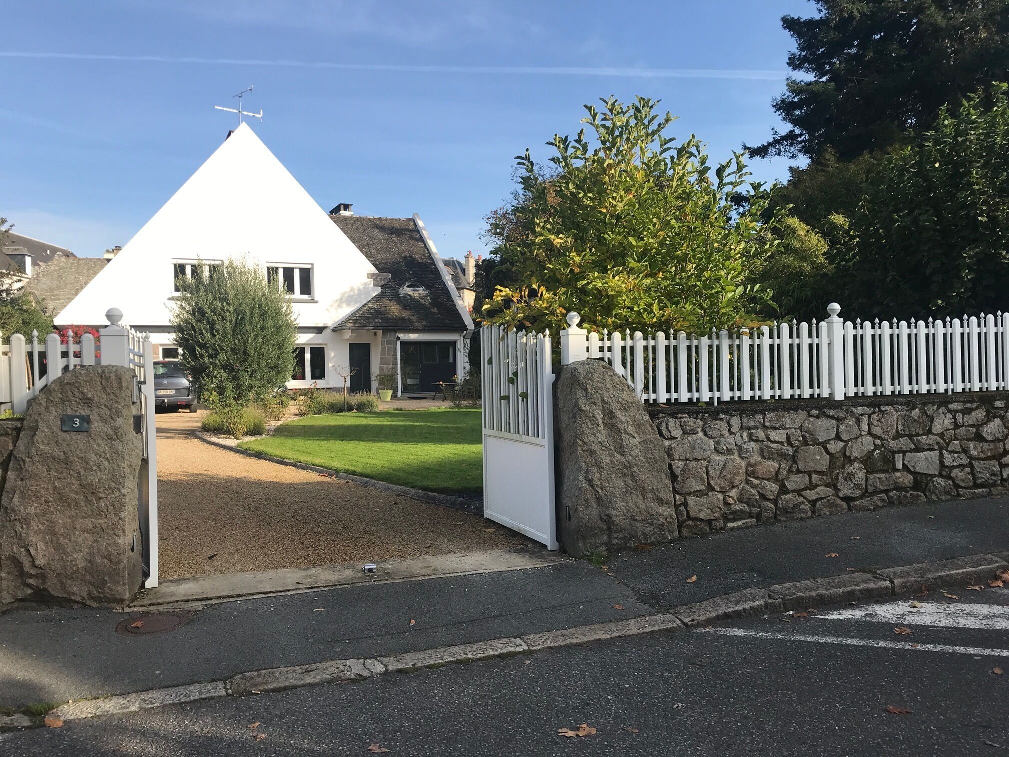 A gated residential area with a white house, stone walls, and a clear sky.