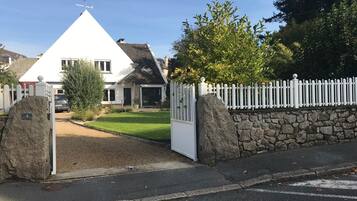 A gated residential area with a white house, stone walls, and a clear sky.