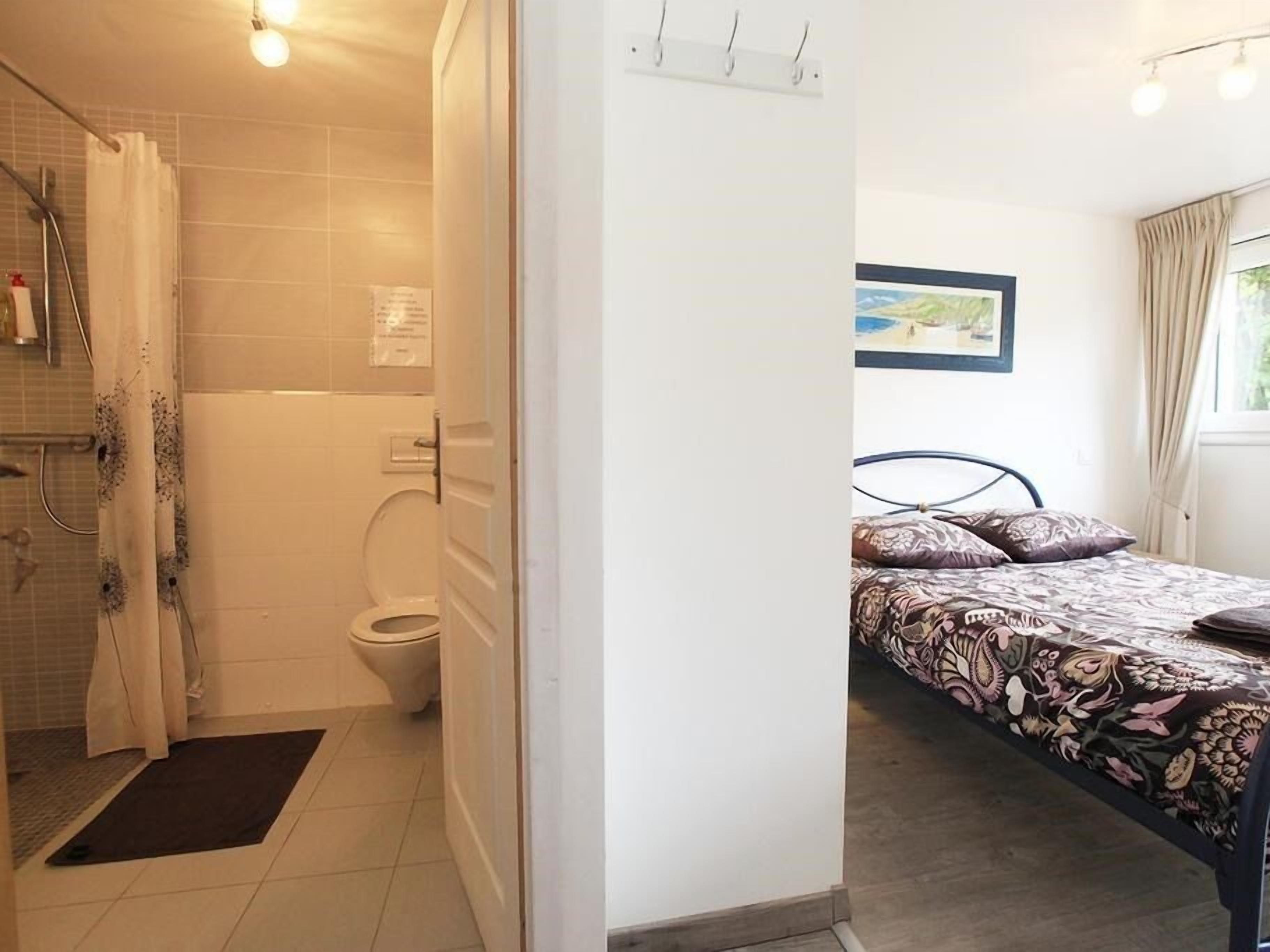 Casa de banho com chuveiro, sanita e cama com colcha estampada.