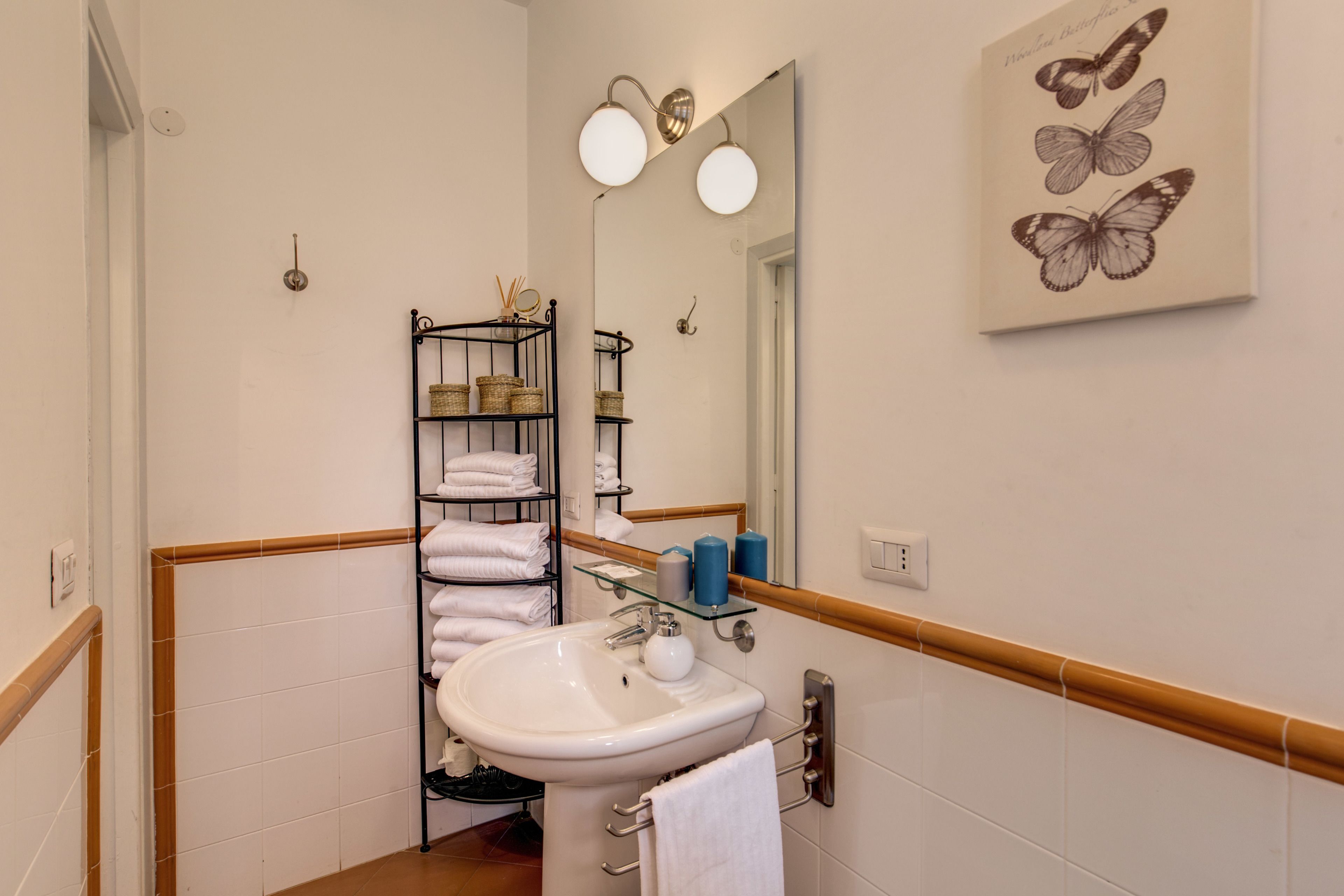 A bathroom with a white sink, mirror, and towel rack. There is a shelf with baskets and toiletries.