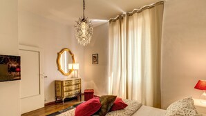 A bedroom with a bed, a dresser, a mirror, a chandelier, and a window with curtains. - Spagna Glamour Life Penthouse (Rome)