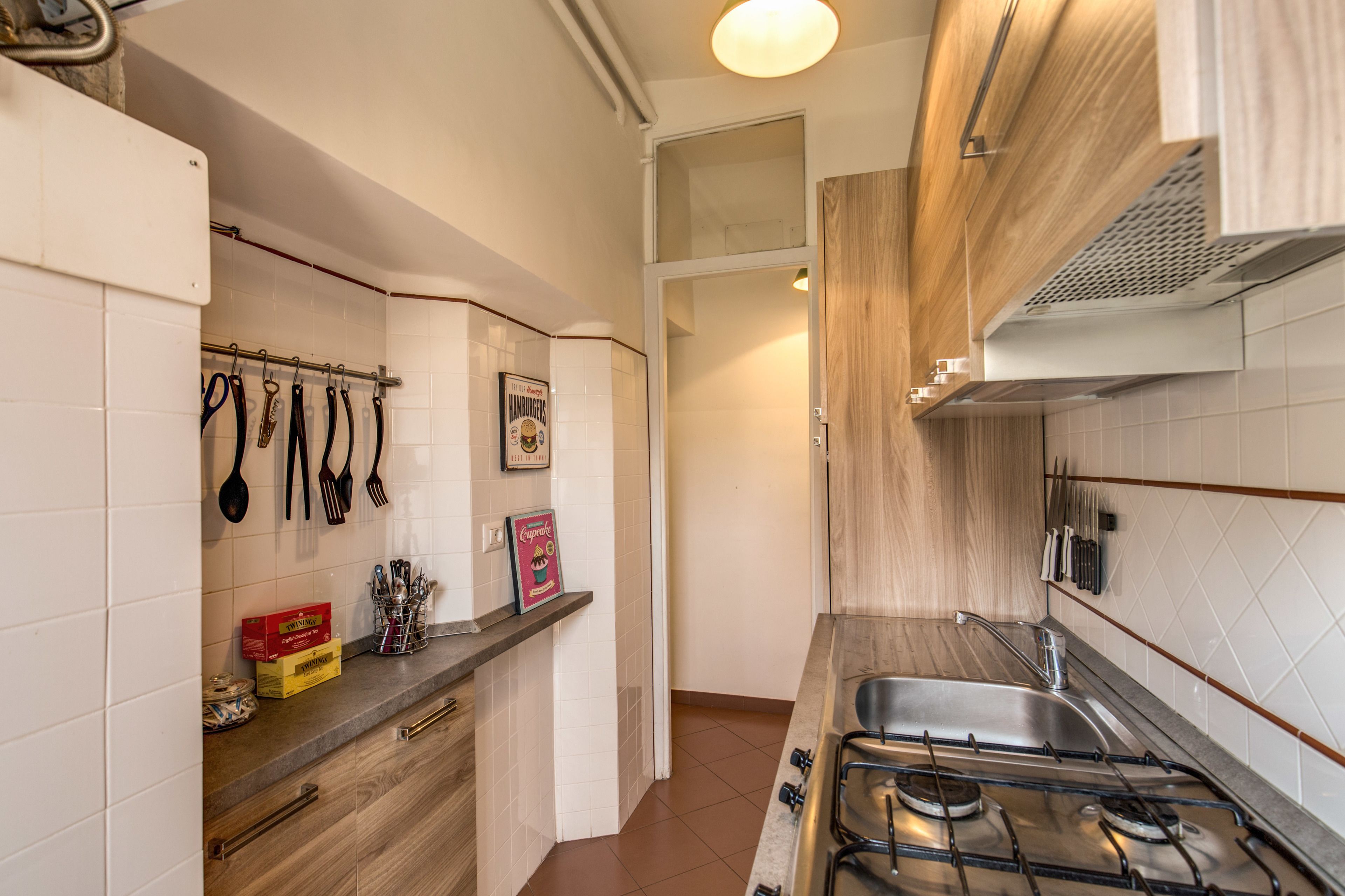 A kitchen with a gas stove, hanging utensils, and a tiled backsplash.