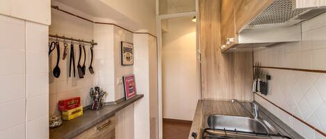 A kitchen with a gas stove, hanging utensils, and a tiled backsplash.